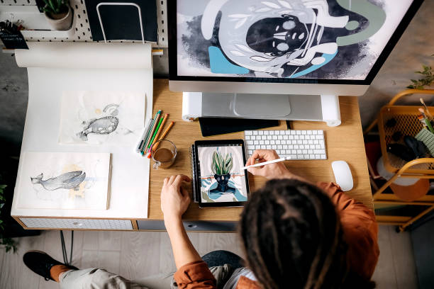 Girl sitting in front of a computer and illustrating on a tablet