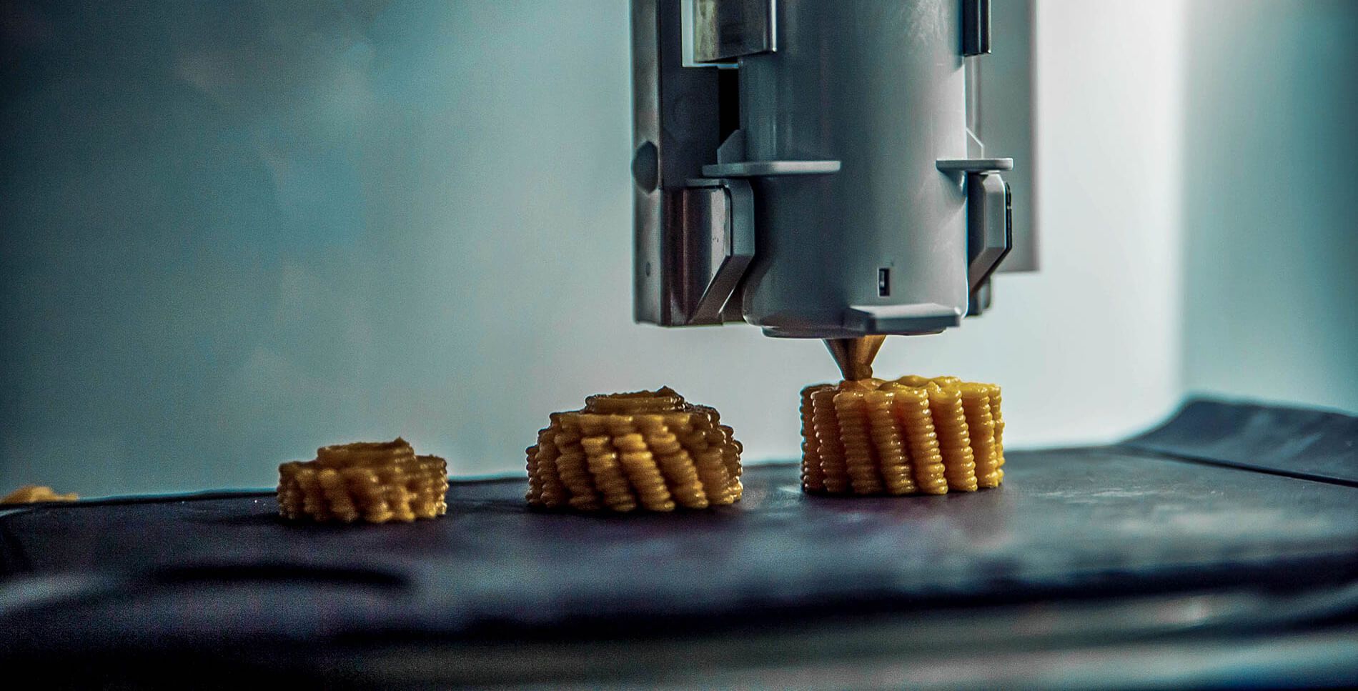 A 3D printer printing 3 renditions of yellow colored food